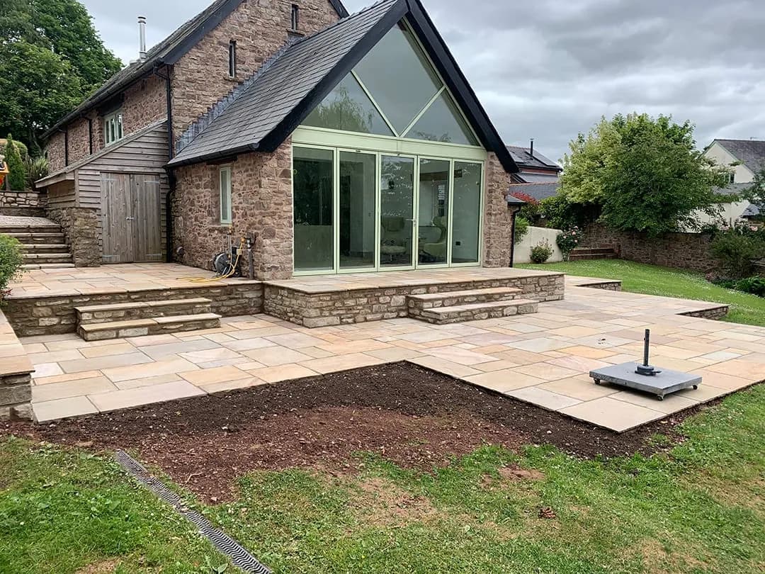 A large sandstone patio with steps behind a stone house with a glazed gable, Monmouthshire