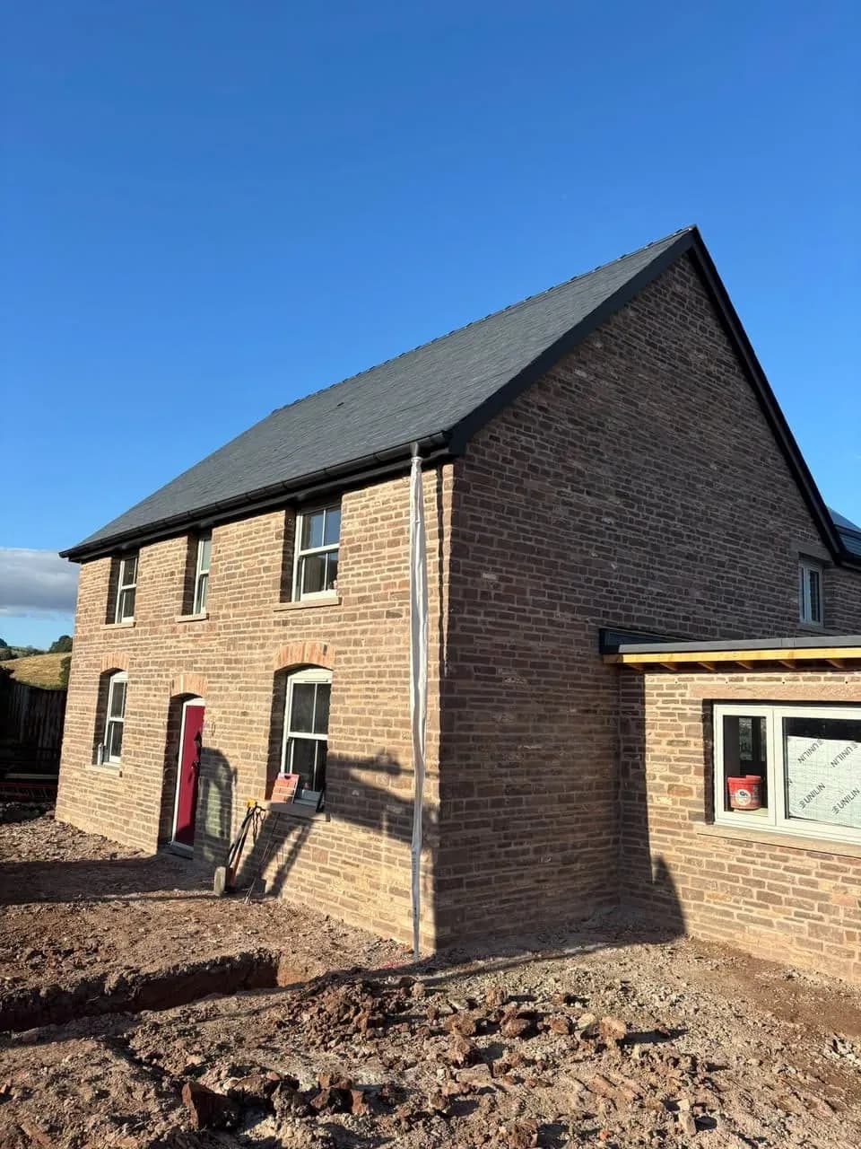 The finished stone farmhouse with its red front door, Cross Ash