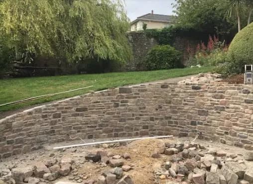 A stone retaining wall being built along the foot of a sloping lawn, Monmouthshire